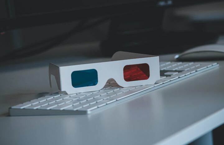 3D glasses sitting on a white keyboard on a white desk.